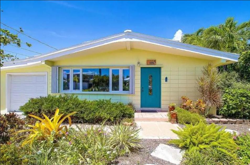 una pequeña casa amarilla con una puerta azul en The Butterfly Cottage en Marathon