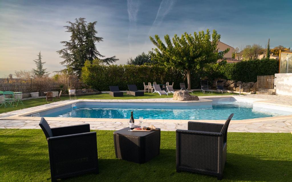 una piscina con sillas y una mesa con una botella de vino en La Halte Gourmande, en Vachères