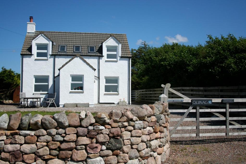 a white house with a stone wall in front of it at Quinag - luxury villa with sea views in Achiltibuie in Achiltibuie