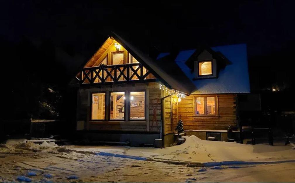 une cabane en rondins éclairée la nuit dans la neige dans l'établissement Chata Kaimówka, à Szczyrk