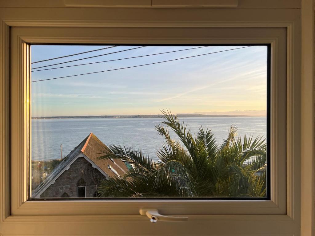 a window with a view of the water and a house at Lookout Cottage in Penzance