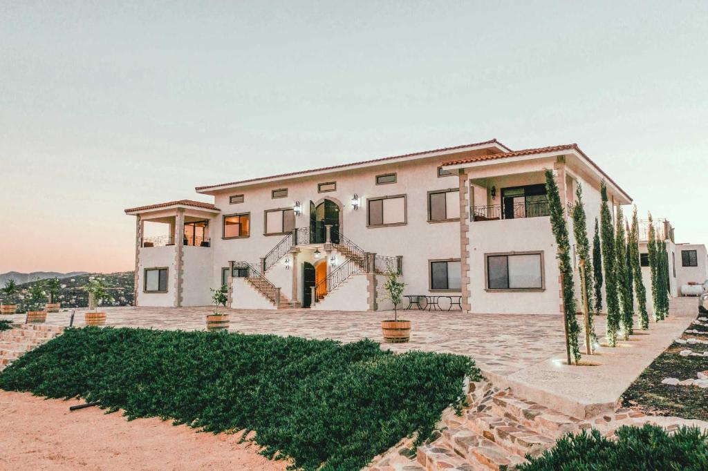 une grande maison blanche avec des arbres devant elle dans l'établissement Villa Montefiori, à Valle de Guadalupe