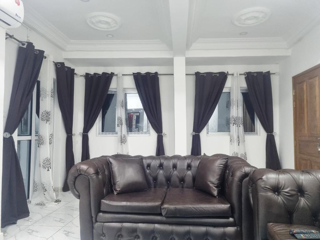 a leather couch in a living room with black curtains at Résidence Sighaka - Suite Royale - WiFi, Gardien, Parking in Douala