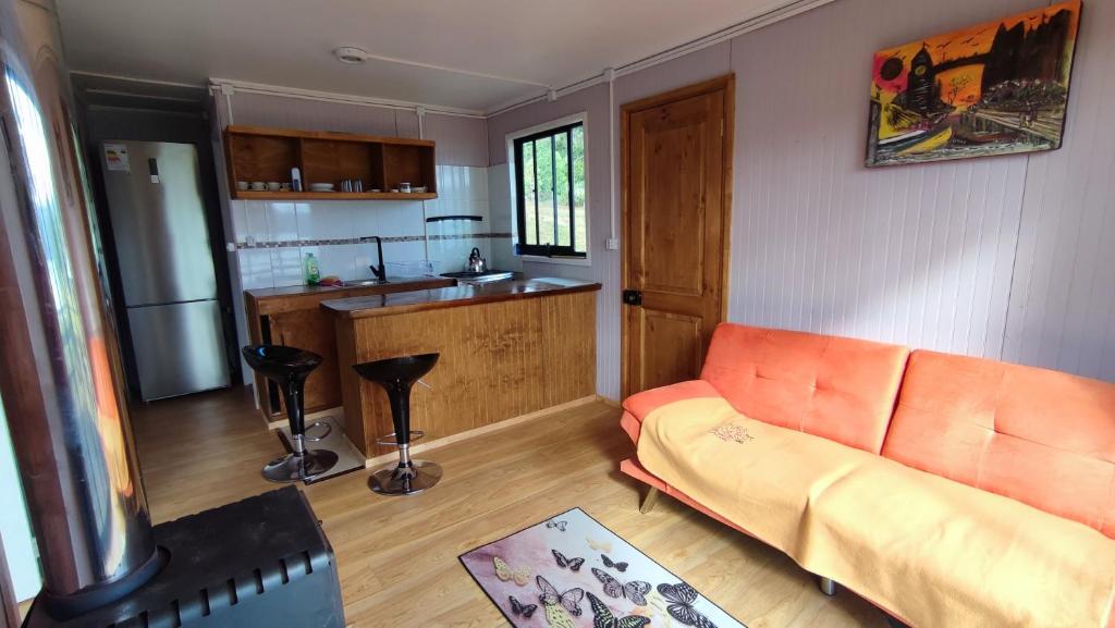 sala de estar con sofá naranja y cocina en Cabañas Isla Del rey, en Valdivia