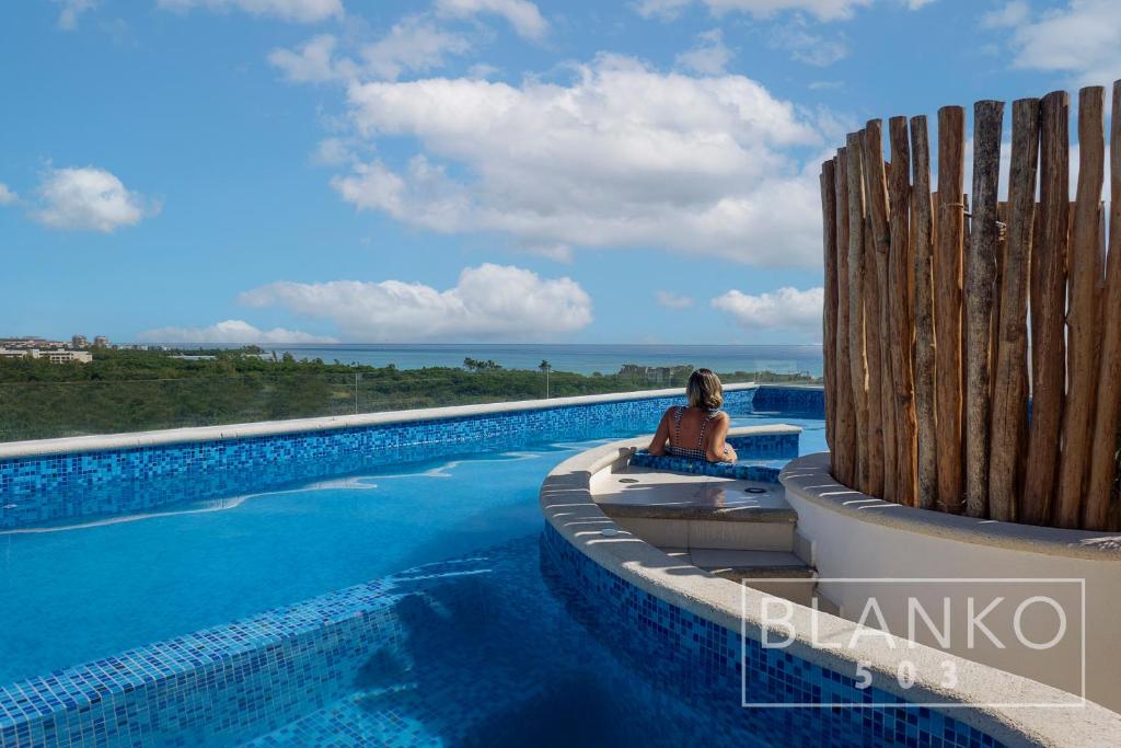 uma mulher sentada numa cadeira ao lado de uma piscina em 5th Av New Luxury Condo - Ocean View em Playa del Carmen