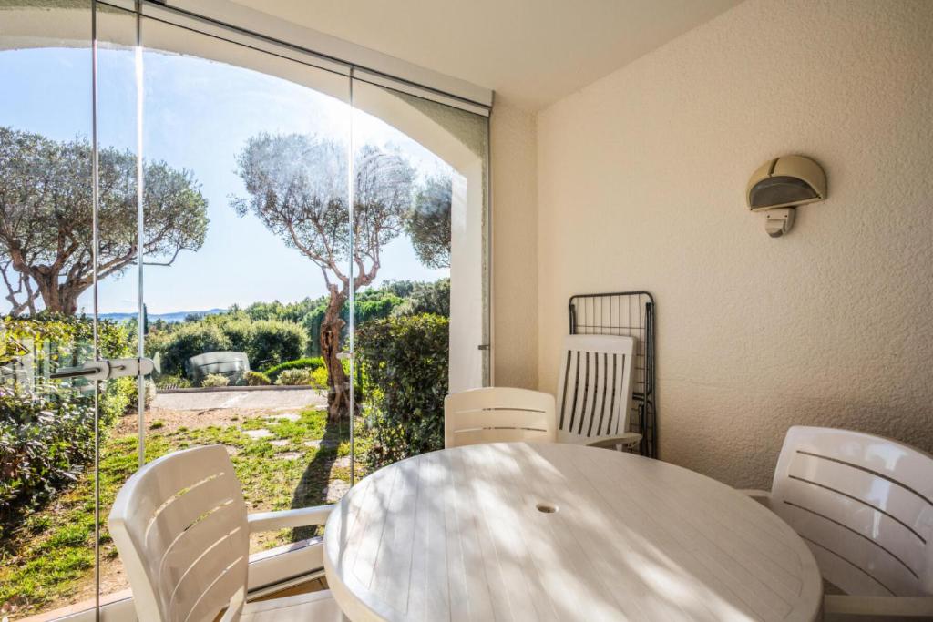 une table blanche et des chaises dans une pièce avec une fenêtre dans l'établissement Les Appartements aux Restanques du Golfe de St Tropez - maeva Home - Appartement spacieux vue mer 2 pièces 5 personnes - Prestige - super Home MAE-2158, à Grimaud
