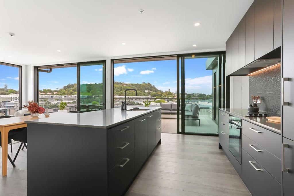 een keuken met grijze kasten en een groot raam bij Enfield Sky - Brand New Luxury Penthouse in Auckland