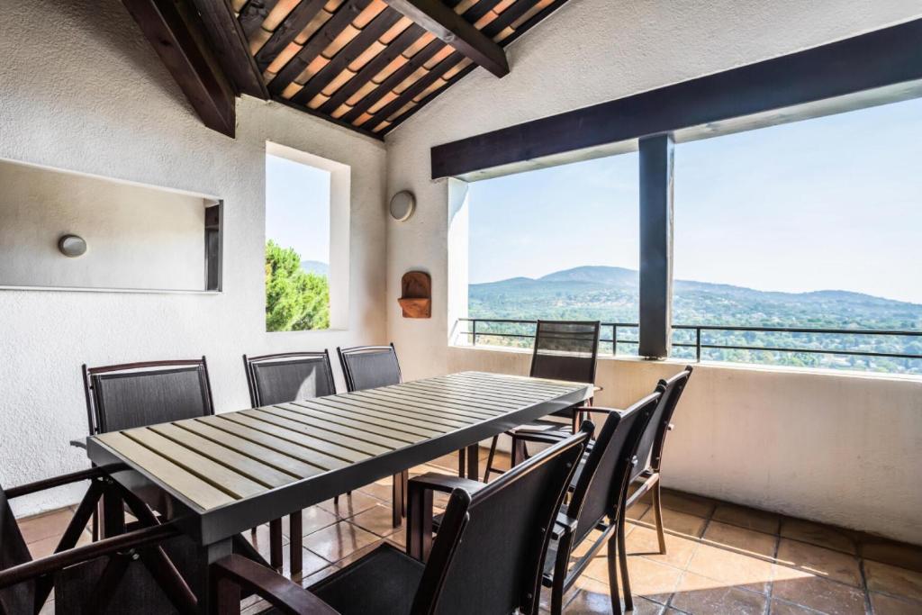 une salle à manger avec une table, des chaises et des fenêtres dans l'établissement Les Bastides aux Restanques du Golfe de St Tropez - maeva Home - Bastide 4 pièces 8 personnes très belle vue mer - Sélection - super Home MAE-5768, à Grimaud
