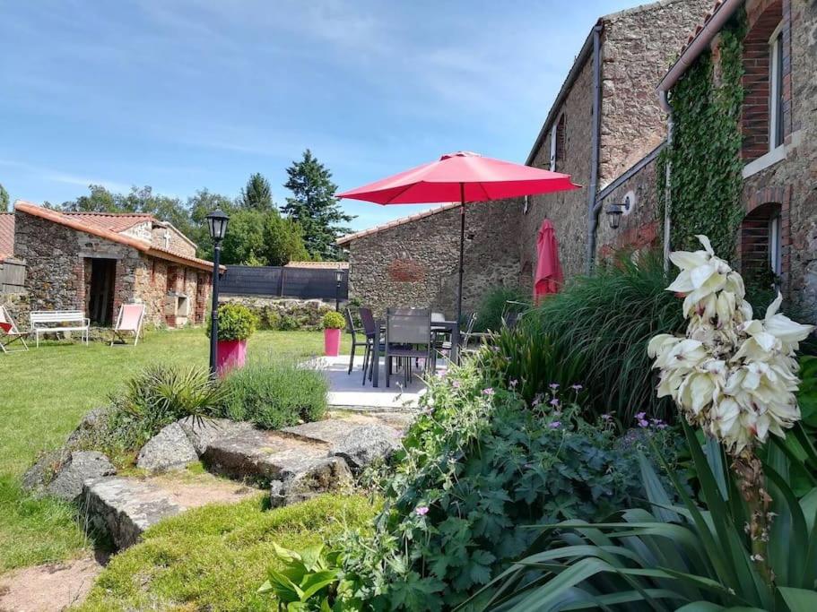 a patio with a table and an umbrella in a garden at L'Ange gîte de groupe proche du Puy du Fou in Sevremont