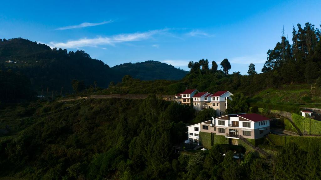 un groupe de maisons sur une colline plantée d'arbres dans l'établissement Dvara Luxury Resort Kodaikanal, à Kodaikānāl