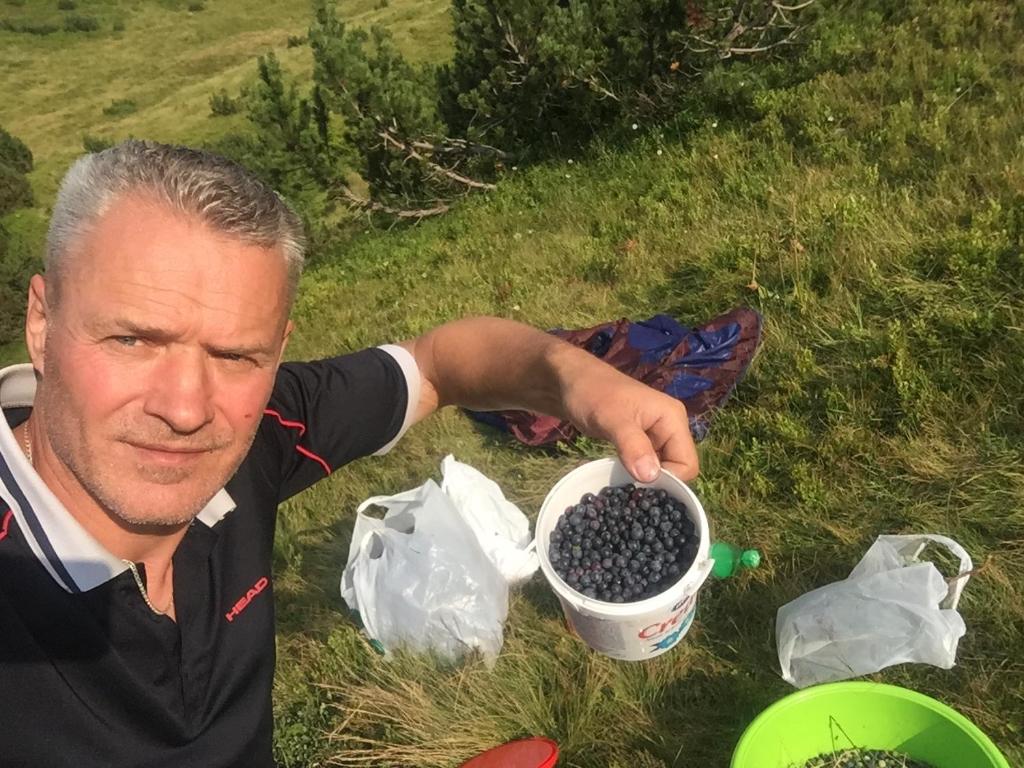 a man sitting on the grass with a bucket of blackberries at Zlatna koliba Namir Zuka in Fojnica