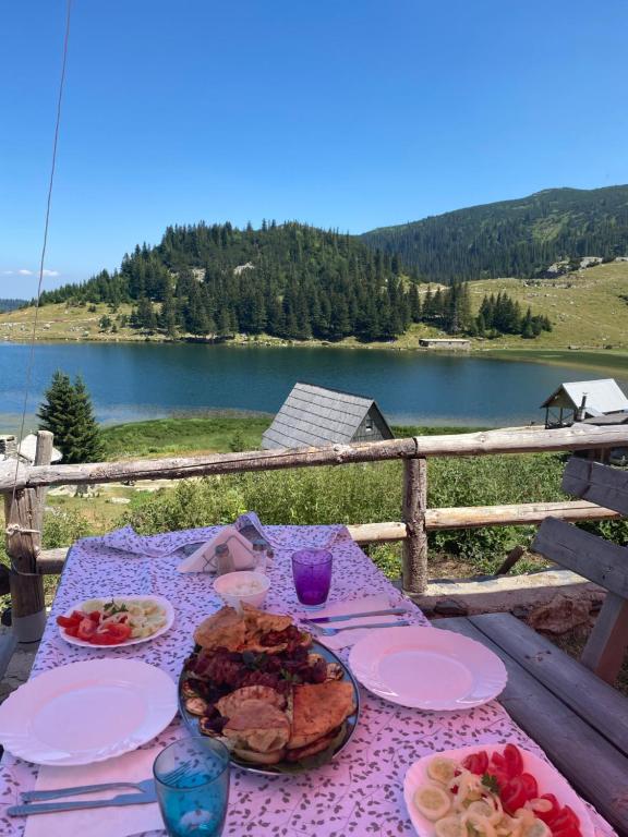 a table with plates of food and a view of a lake at Zlatna koliba Namir Zuka in Fojnica