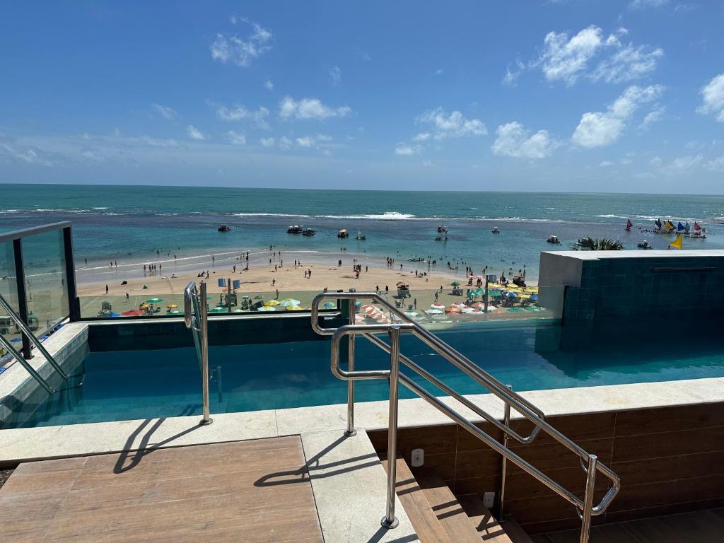 - une piscine à côté d'une plage avec des gens dans l'eau dans l'établissement Porto Galinhas frente mar Mikonos, à Ipojuca