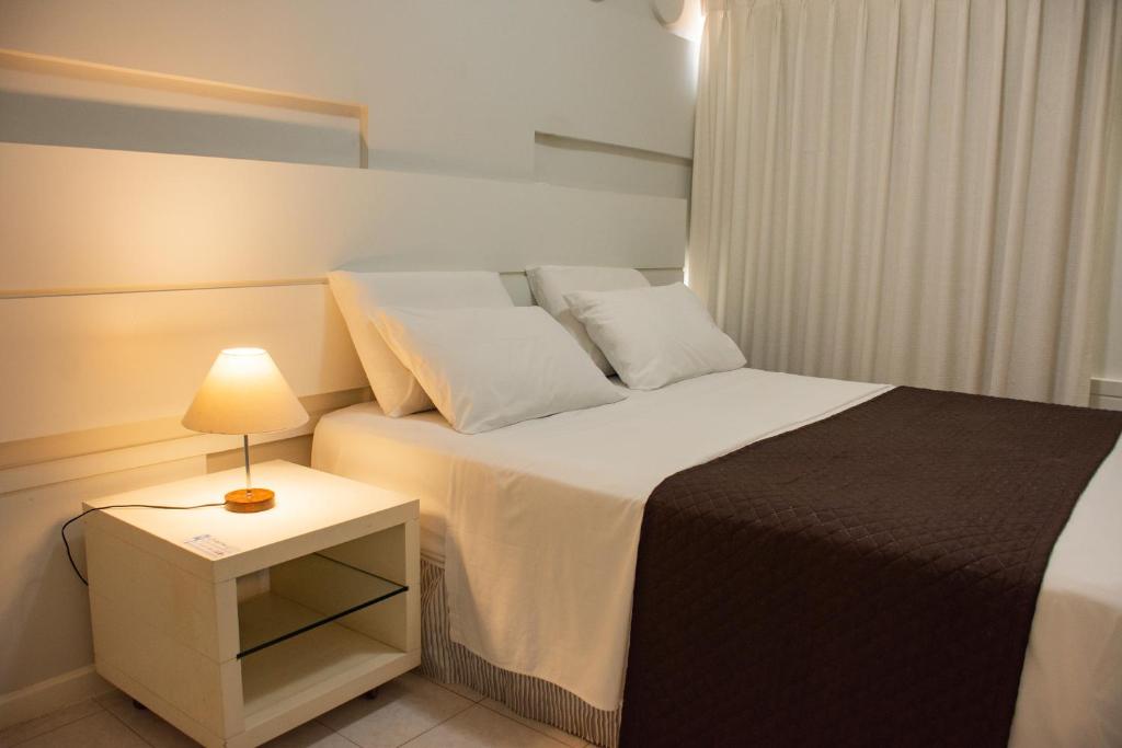 a bedroom with a bed and a night stand with a lamp at Classe Apart Hotel in Feira de Santana