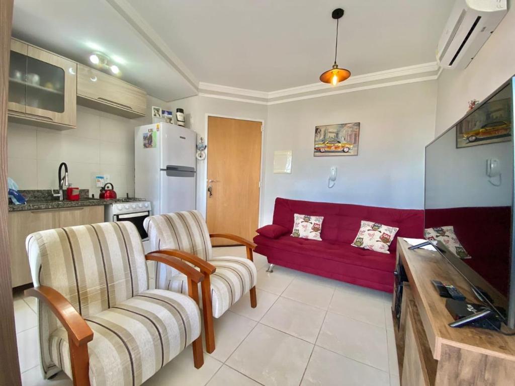 a kitchen and a living room with a red couch at Pé na areia em Capão in Capão da Canoa
