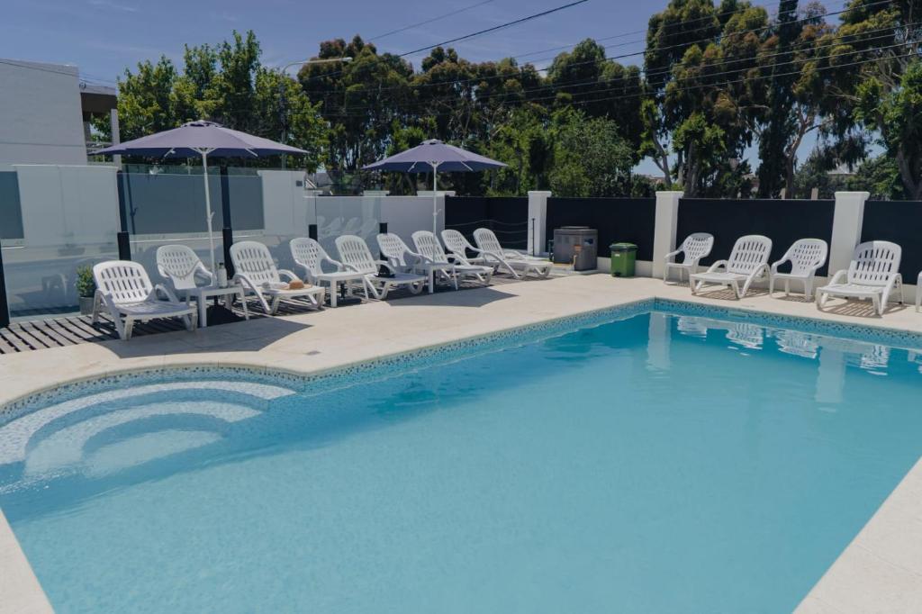 uma piscina com cadeiras brancas e guarda-sóis em Saint Uriel em Puerto Madryn