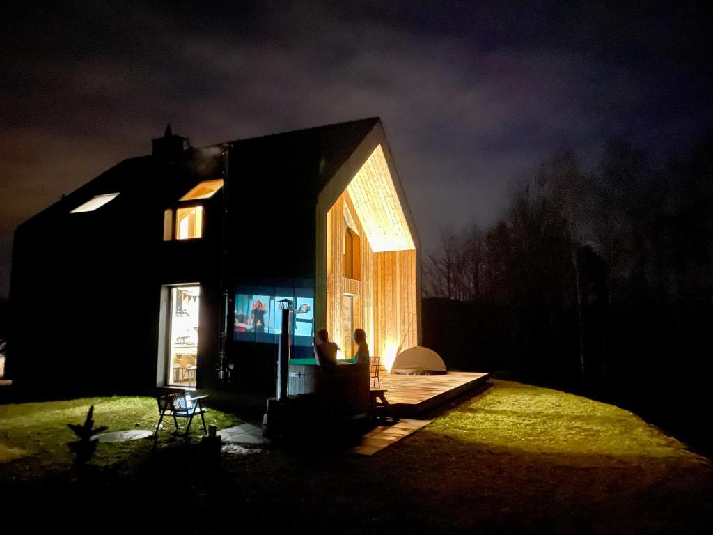 una casa iluminada por la noche con dos personas sentadas afuera en Drwalówka - Domek "NA SKARPIE", en Grzechynia