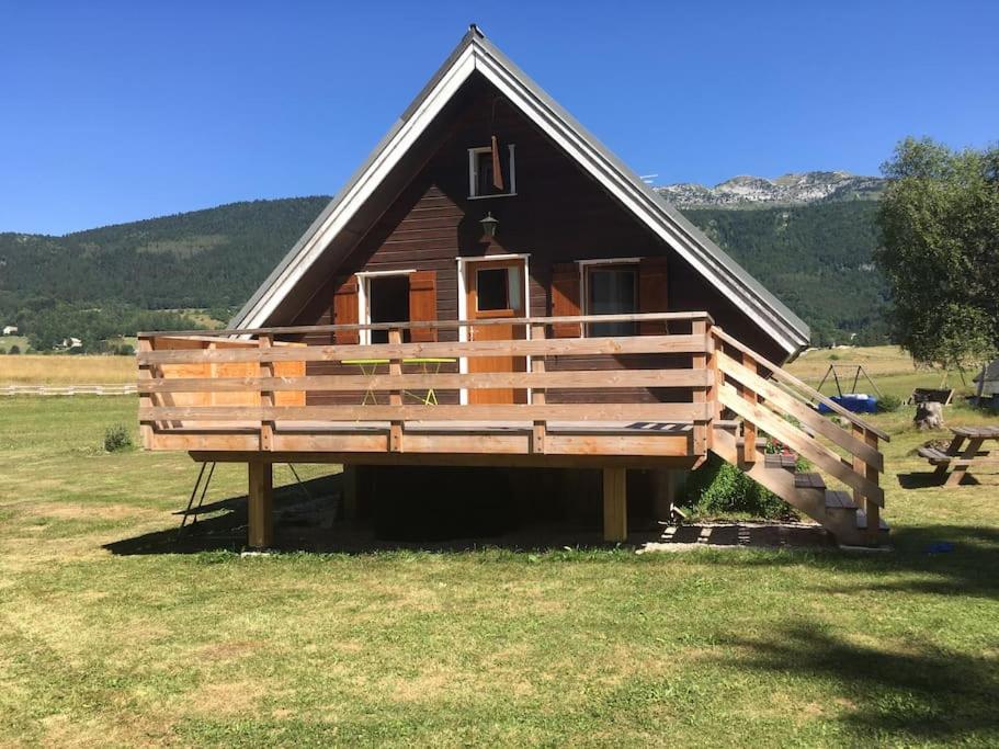 una pequeña casa con una gran terraza en un campo en Chalet cosy, belle vue, dans le massif du Vercors, en Lans-en-Vercors