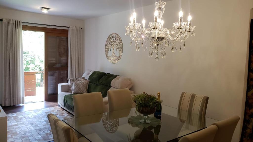 ein Esszimmer mit einem Glastisch und einem Kronleuchter in der Unterkunft Apto 3 Quartos Centro Gramado in Gramado