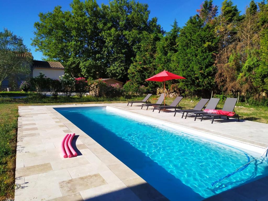 uma piscina com cadeiras e um guarda-sol vermelho em DOMAINE LA MASQUIERETTE em Villepinte