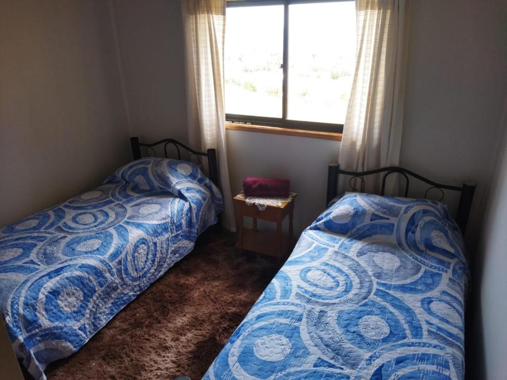 2 Betten in einem kleinen Zimmer mit Fenster in der Unterkunft Cabaña Los Lagos in Puerto Montt