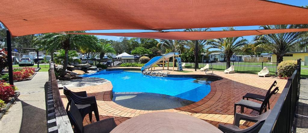 an umbrella over a swimming pool with a slide at Sunset Caravan Park Woolgoolga in Woolgoolga