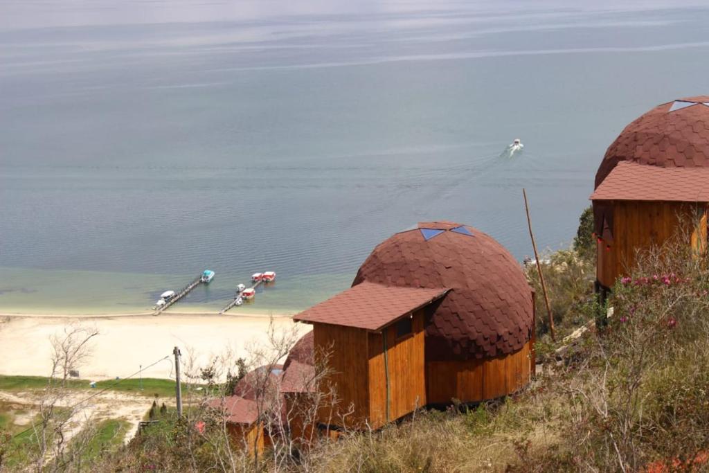 twee kleine hutten op een heuvel naast een strand bij Lago de Tota Playa Blanca-Glamping Kairos in Tota