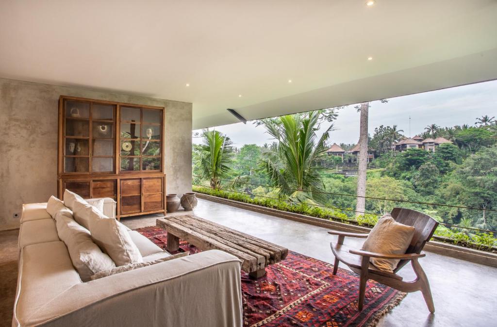een woonkamer met een bank en stoelen en een groot raam bij Hidden Gem Suites Ubud in Ubud