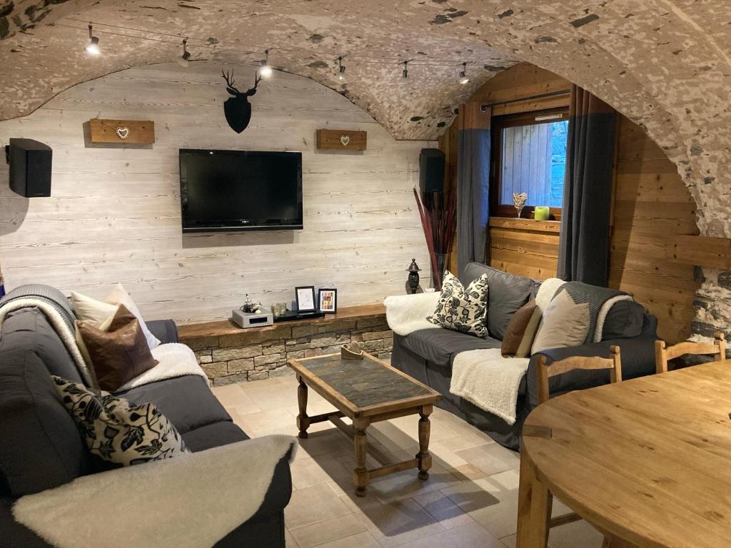 a living room with couches and a tv on a wall at Two Bedroom Apartment La Voute, Chandon near Meribel - Sleeps 4 Adults or 2 Adults and 3 Children in Les Allues