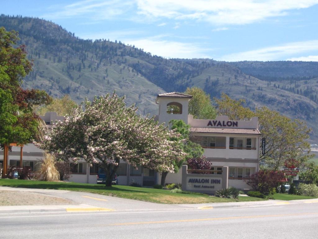 a building with a tree in front of a mountain at Avalon Inn in Osoyoos
