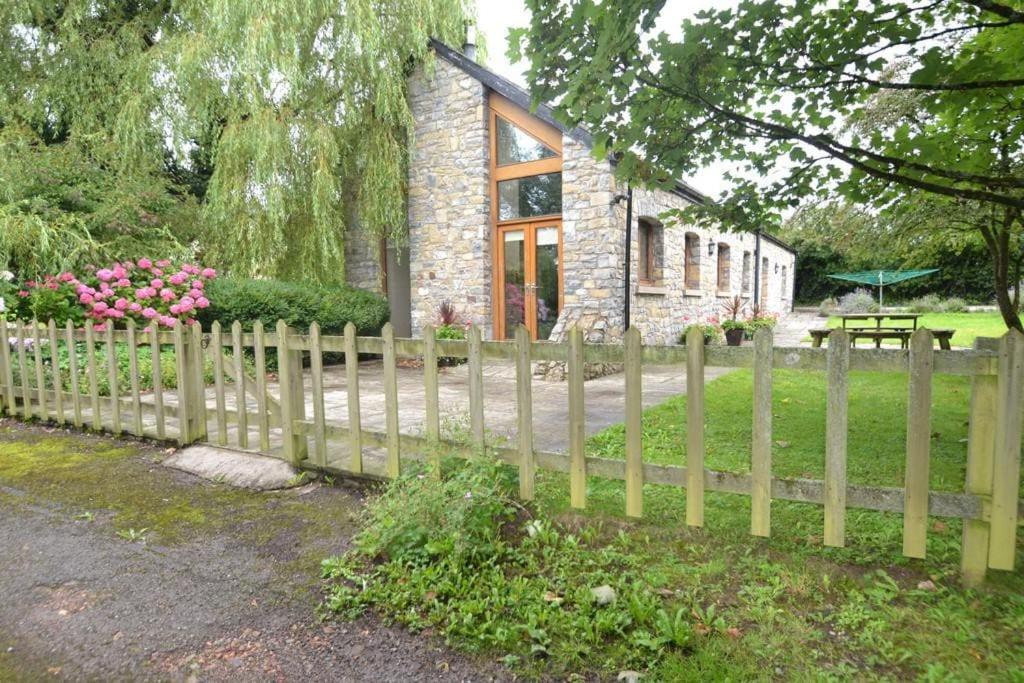 une clôture en bois devant une maison en pierre dans l'établissement Heronston Barn Cottage, à Bridgend