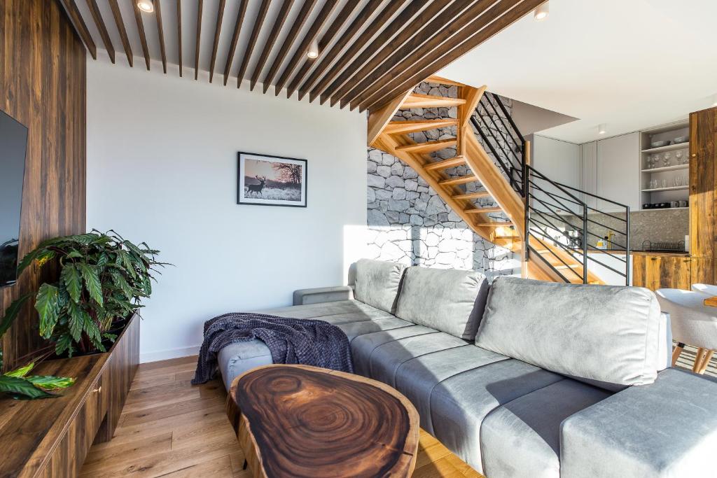 Spacious living room with gray sectional, wooden beam ceiling, stone wall and staircase, warm natural light.