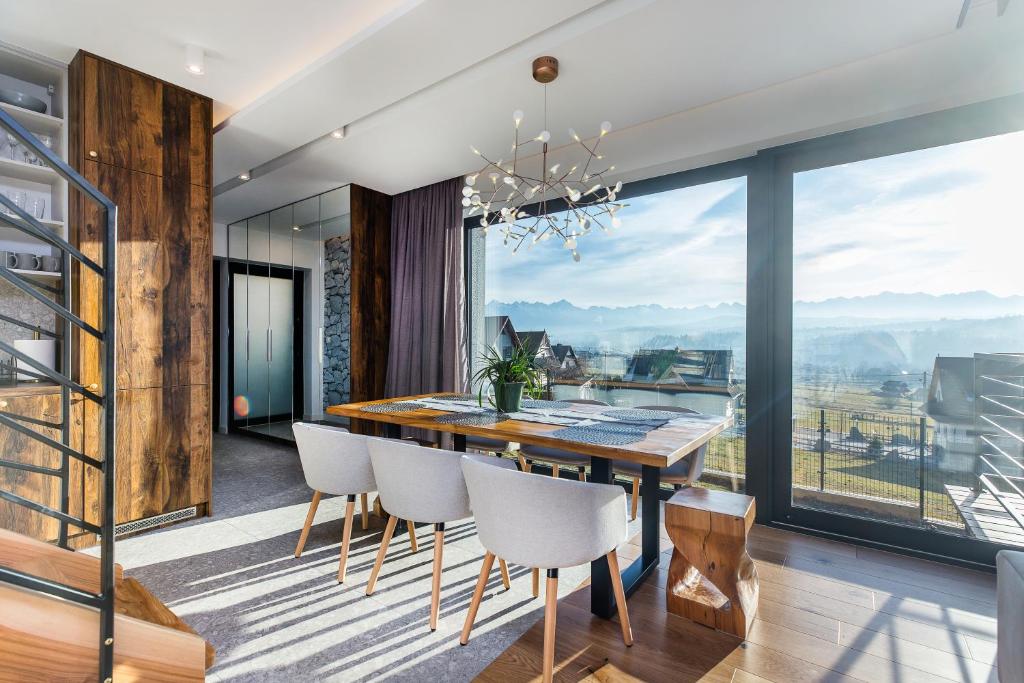 Bright dining space with wooden table, upholstered chairs and panoramic windows showing countryside view.
