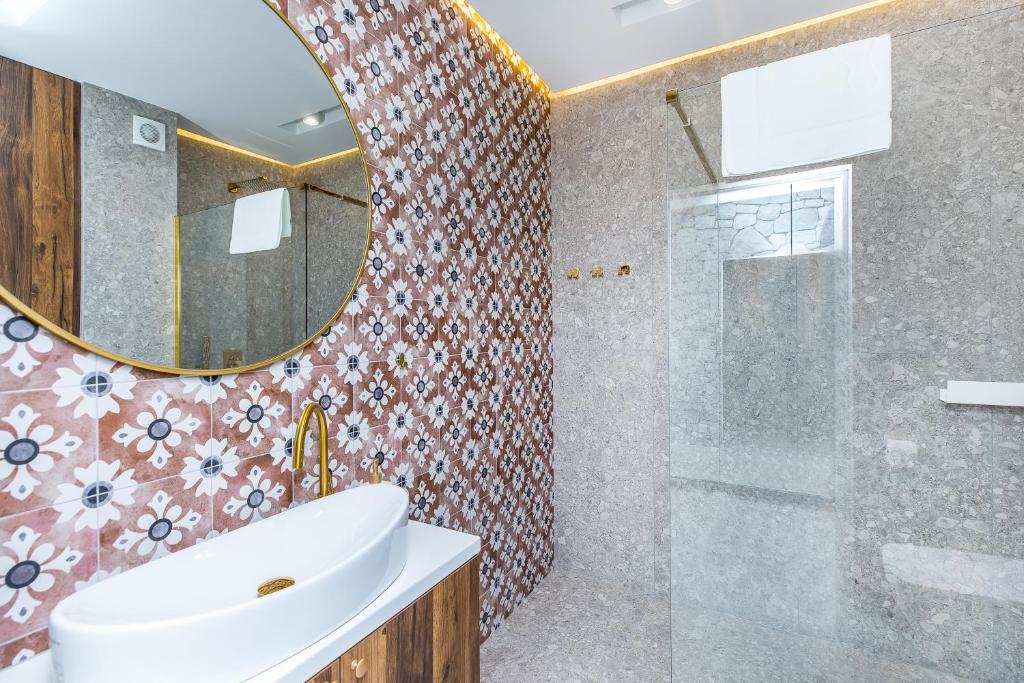 Bathroom with floral patterned tiles, round mirror, white vessel sink and glass-enclosed shower, elegant brass fixtures.
