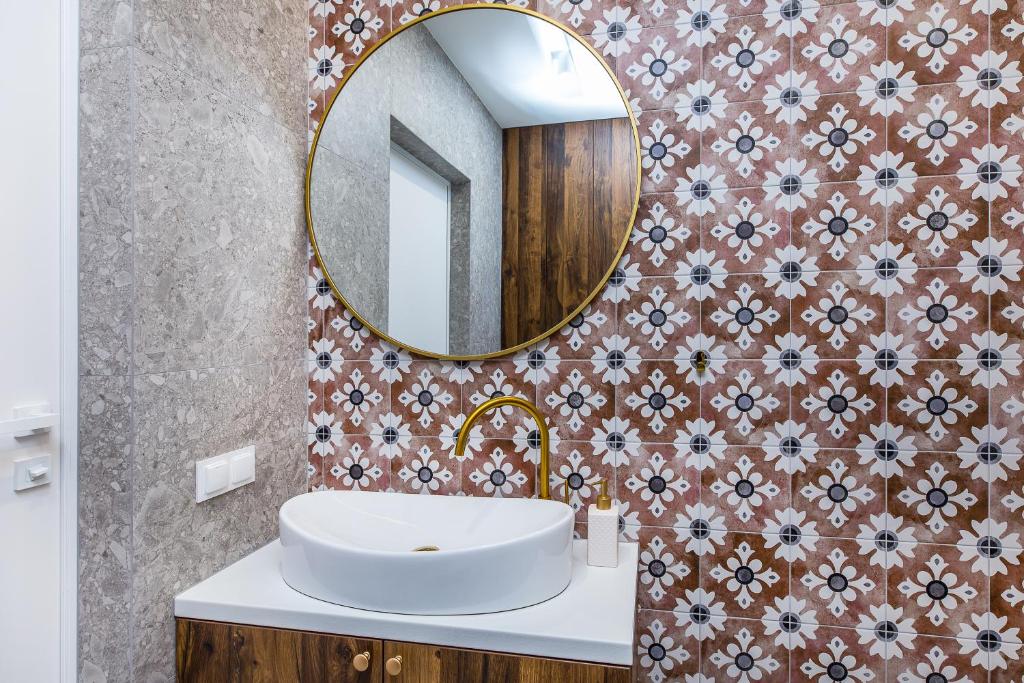 Round mirror above white vessel sink, patterned tile wall and gold faucet on wood vanity.