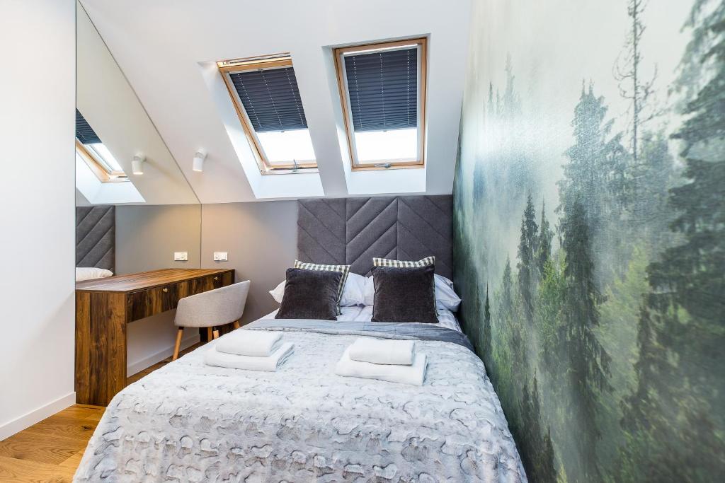 Bed beside mirrored wall and wooden desk, skylights overhead and a misty forest mural.