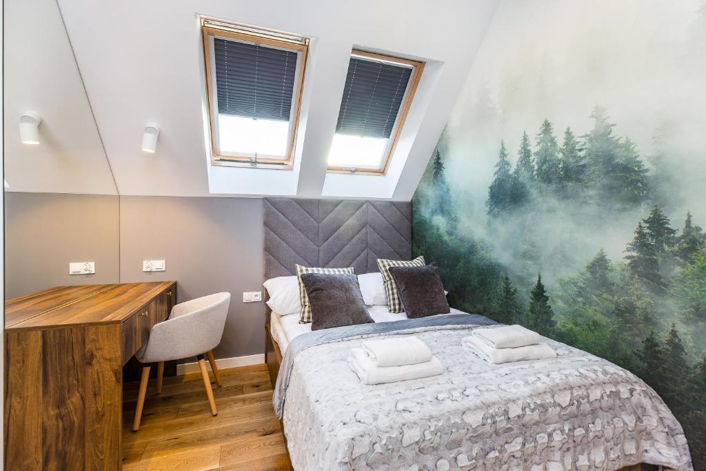 Compact attic bedroom with double bed, wooden desk, skylights and large forest-themed wall mural.