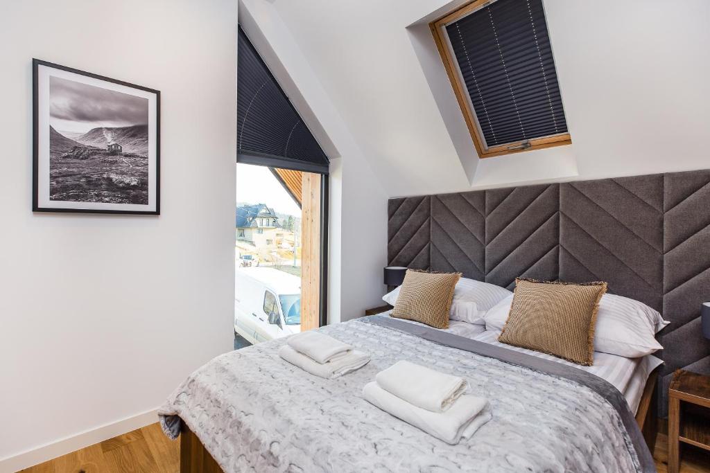 Well-lit bedroom with angled window, grey padded headboard, textured bedding and decorative pillows.