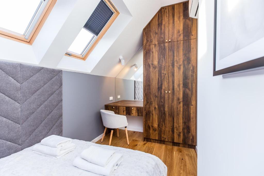 Bright attic bedroom with skylights, grey upholstered headboard, wooden wardrobe and small vanity desk.