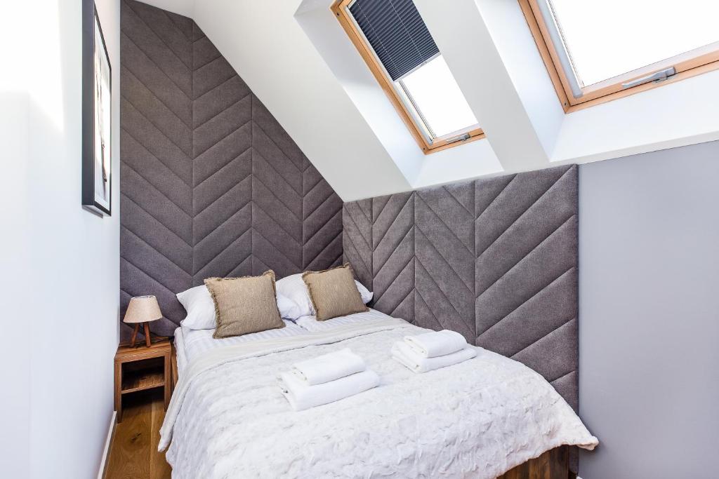 Small double bed under skylights with chevron grey upholstered headboard and folded towels.