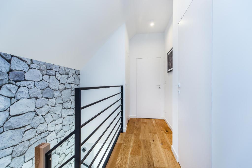 Upper-floor hallway with black metal railing, stone textured wall and hardwood flooring leading to white door.