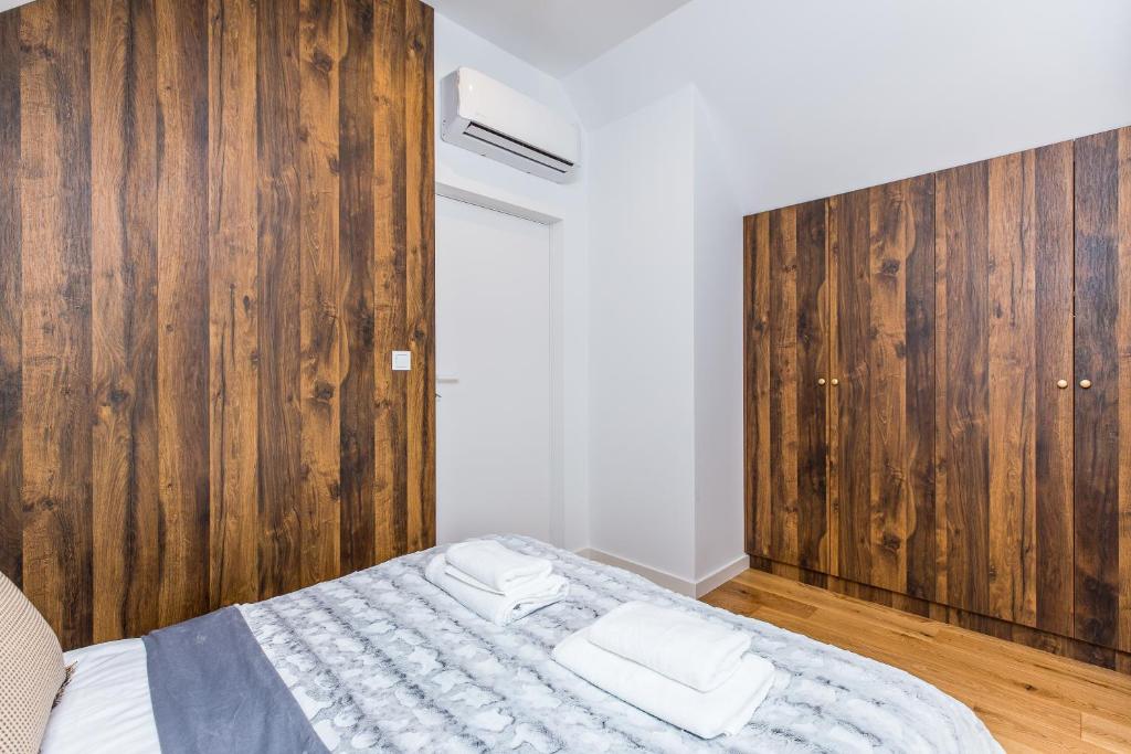 Cozy bedroom corner with folded towels on bed, wood-paneled wardrobes and air conditioner above door.