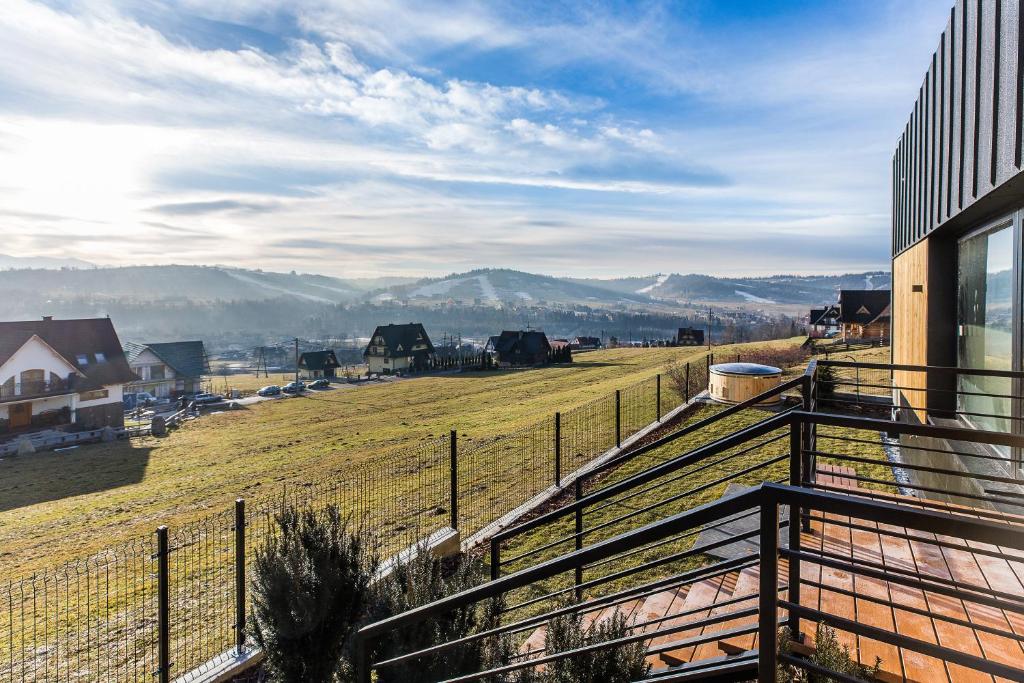 Balcony view over grassy hillside and scattered houses, metal railings, cloudy blue sky and distant hills.