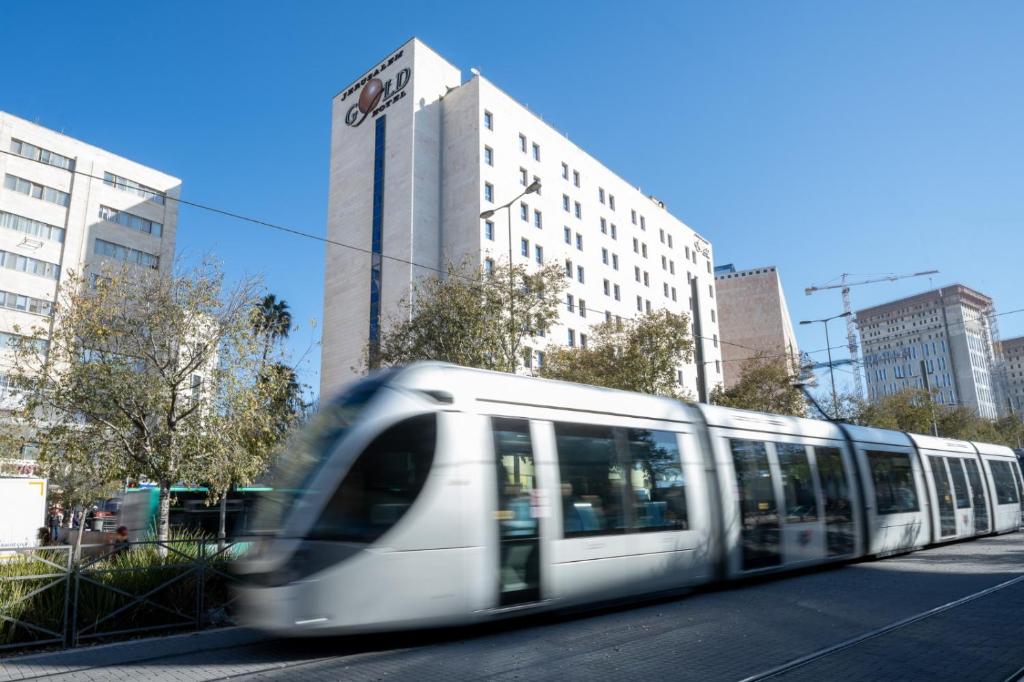 un tren blanco viajando por una calle de la ciudad con edificios en Jerusalem Gold Hotel en Jerusalén