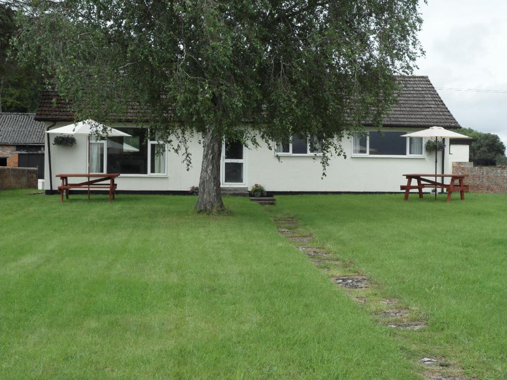 a house with two picnic tables and a tree at Bungalow in lovely setting.Ten minutes to Longleat in North Bradley