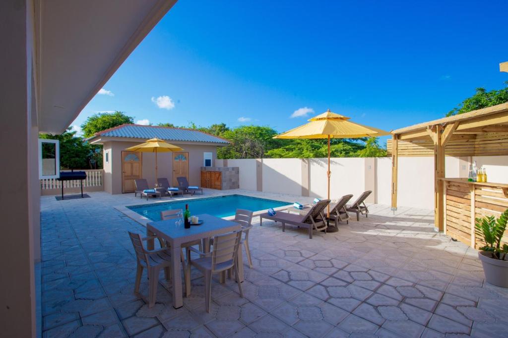 a patio with a pool and tables and chairs and umbrellas at Lovely Caribbean family villa with private pool in Willemstad