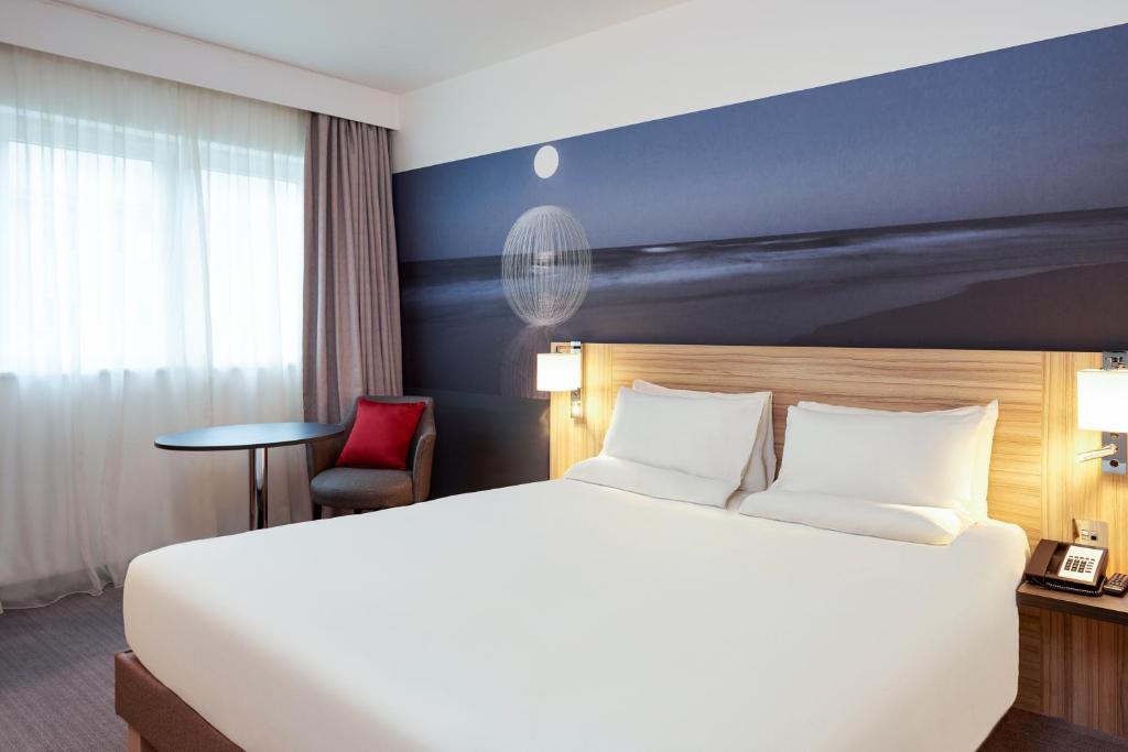 a hotel room with a large bed and a red chair at Novotel London Stansted Airport in Stansted Mountfitchet