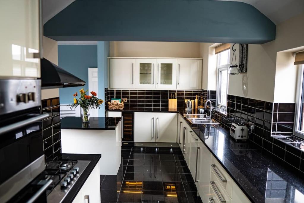 a kitchen with white cabinets and black tile walls at Spacious Family Home Minutes from the Beach in Blackpool