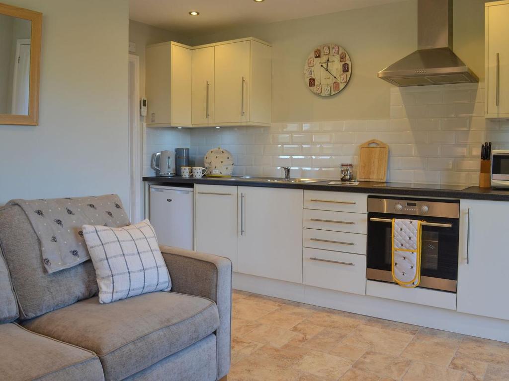a kitchen with white cabinets and a couch and an oven at The Honey House in Eastry