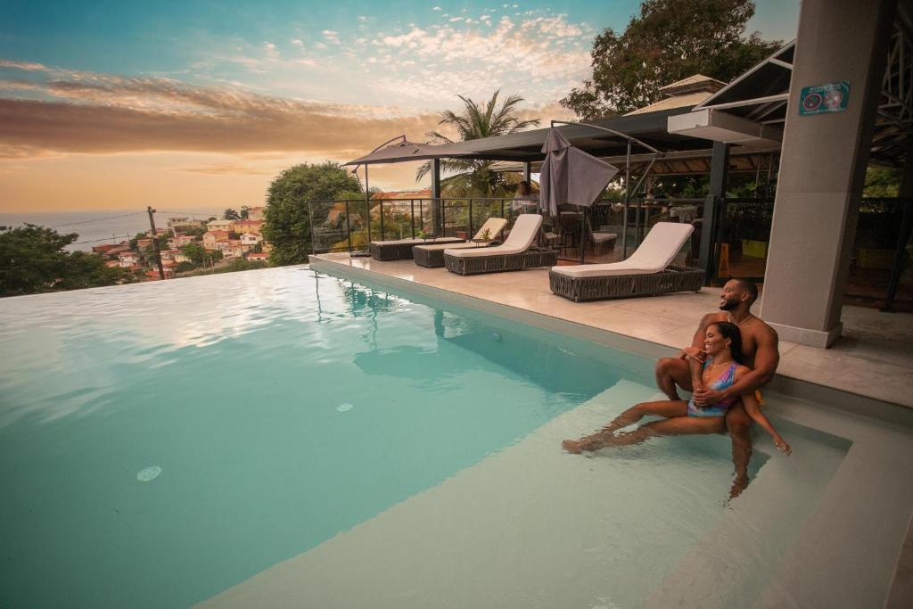 a man and woman sitting on the edge of a swimming pool at Karibea Squash Hôtel in Fort-de-France